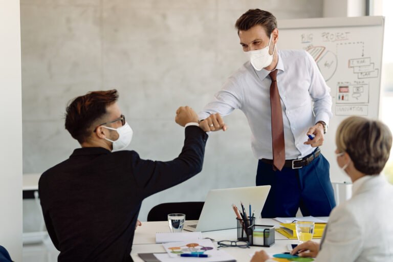 Happy businessman with protective face mask greeting with his colleague on a meeting in the office.