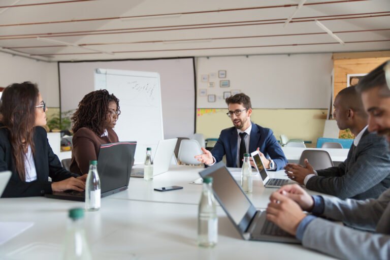 Focused boss communicating with workers. Thoughtful employees sitting at table during morning briefing. Business meeting concept